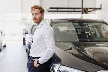 Naklejka na ściany i meble Confident pensive man customer buyer businessman client wears white shirt chooses auto wants to buy new automobile in car showroom vehicle salon dealership store motor show indoor. Car sales concept