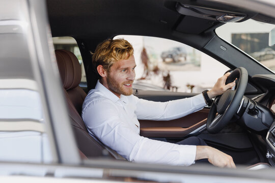 Side view confident happy man customer buyer client wearing shirt sit in car salon drive chooses auto wants buy new automobile in showroom vehicle dealership store motor show indoor Sales concept
