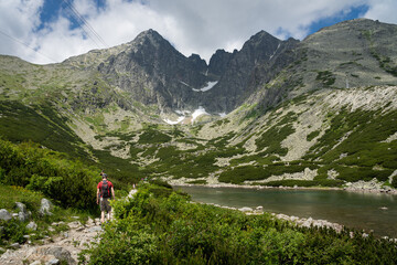 Fototapeta na wymiar Adult man with a backpack hiking along Skalnate Pleso (Rocky Tarn) in High Tatra mountains, Slovakia. A cable car heading to Lomnicky Stit peak. Beautiful clean nature in Central Europe
