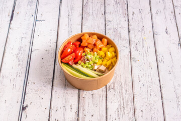 Marinated Norwegian salmon poke bowl with pieces of mango, tofu, cucumber in strips, cherry tomatoes and chopped chives