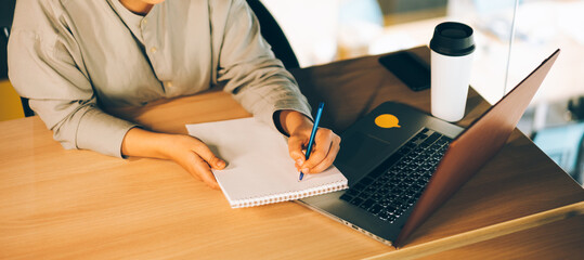 A woman in glasses studying online with her laptop, writing in notepad. Easy online education with computer and eLearning webinars concept