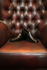 black leather shoes are placed on a maroon luxury chair