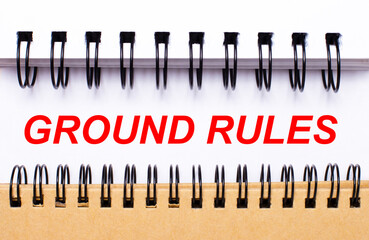 Text GROUND RULES on white paper between white and brown spiral notepads.