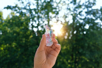 beautiful aura quartz crystal in hand, sunny natural forest background. Esoteric spiritual...