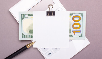 On a light gray background, a white calculator, cash dollars and paper with a place to insert text. Template. Business concept