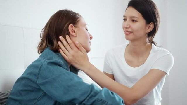 A positive lesbian couple are looking at each other while hugging sitting together at the bedroom