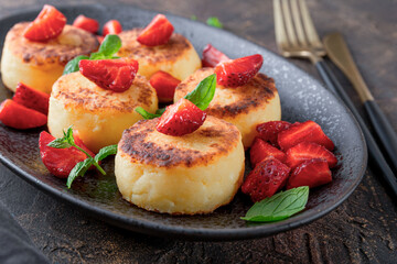  Cottage cheese pancakes with strawberries and mint on a black plate on the dark table close up