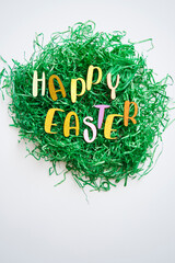 Easter nest of artificial grass on white background with letters saying "Happy Easter" and space for copy text.