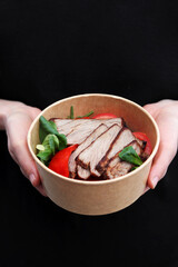 Female hands hold food delivery box having lunch at work from home office. Daily healthy meal weight loss diet menu on black background.