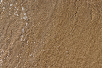 Fototapeta na wymiar Wave flooded sea coast with bubbles and ripples