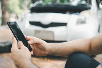 Asian man using smartphone for assistance after a car breakdown on street. Concept of vehicle engine problem or accident and emergency help from Professional mechanic