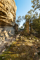 imagen de una pared de roca junto a un pequeño camino y unas paredes de una casa derruida 