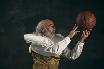 One old man, actor having fun, playing with basketball ball isolated on dark vintage background. Retro style, comparison of eras concept.