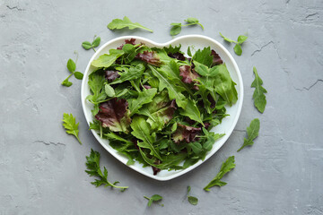 Fresh salad mixture of arugula leaves, mizuna lettuce, peas and lollo rosso on a gray concrete background. Concept: healthy food, top view.