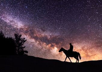Silhouette of a lone rider on a horse standing on a hill in the starry night. Behind him is the...