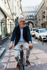 smiling mature man listening music in earphones and riding bicycle