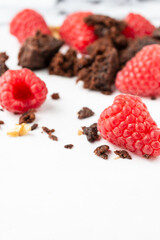 Close-up of pieces of chocolate brownie with crumbs, walnuts and red raspberries, selective focus, on white table, vertical, with copy space