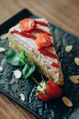 A Slice of Healthy Strawberry Cake with Fruits and Nuts on the Black Plate in a Caffe or Restaurant
