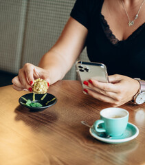 Fototapeta na wymiar An Anonymous Woman Eating Healthy Protein Ball with Pistachios and Drinking Cup of Espresso Coffee while Using Mobile Phone in a Cafe