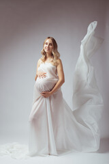 Elegant pregnant young woman standing wearing light fabric. Pregnancy, fantasy and fairy tale concept.