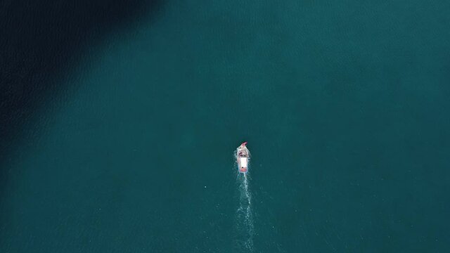 Aerial view. Beautiful shot of the colorful fishing boat going to the port. Tranquil seawater with a moving shadow of the cloud. Amazing top-down drone view. 