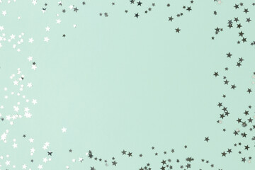 Border frame made of silver colored stars confetti on a turquoise background.