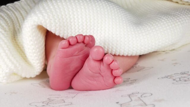 Close up shot of newborn baby in diaper lying on back and jerking her small legs