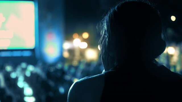 Sitting woman watching football in a public place at night