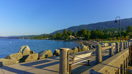 Obraz premium Dundarave pier on a summer morning with palm trees in park and Cypress mountain on right and view across Burrard Inlet bay