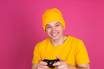 European handsome young man in yellow t shirt on pink background gamer with joystick playing games happy smiling  cheerful