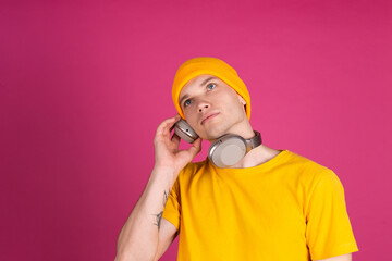 European handsome young man in yellow t shirt on pink background with wireless headphones