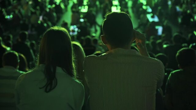 Sitting couple watching football in a public place and talking at night