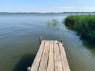 Obraz premium Beautiful picturesque outdoor scene of an old wooden pier sticking out into the calm water of Volga River with reeds and grasses in summer