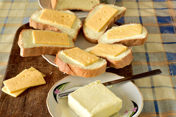 On a cutting board there is a plate on which sandwiches are laid, consisting of bread, cheese, butter.