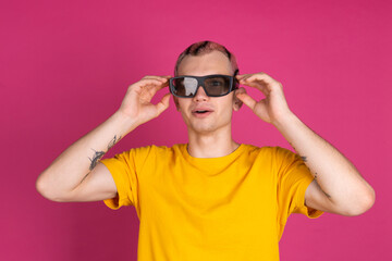 European handsome young man in yellow t shirt on pink background with 3 d cinema glasses