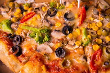 Baked pizza with ham, corn, broccoli, olives, tomato. Unhealthy fastfood junk food favorites by young people.