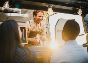 Cheerful food truck seller speaking with multiethnic couple