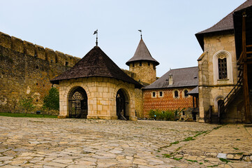 Fototapeta na wymiar Amazing landscape view of courtyard with ancient stone buildings in the medieval castle. High stone wall with tower in the background. Famous touristic place and romantic travel destination