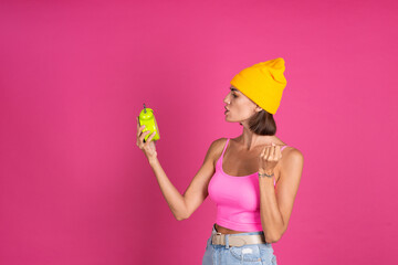Bright portrait of woman in yellow hat on pink  background with alarm clock angry shouting, tired, sleepless