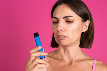 Bright portrait of young beautiful woman on pink background smoking electronic cigarette, looks at...