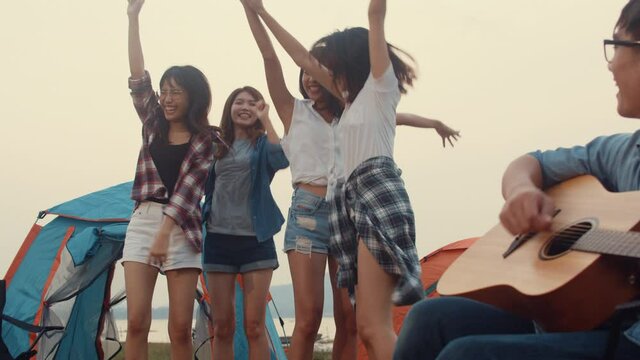 Group of Asia best friends teenagers give high five and dancing enjoy with guitar music happy moments together beside tents in national park. On the background beautiful nature, mountains and lake.