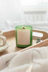 Soy candle and a cup of coffee on a tray. The tray is on a light white bed.