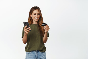 Image of smiling middle aged woman, reading credit card number, fill in info on mobile phone app, paying online, do shopping on smartphone, white background