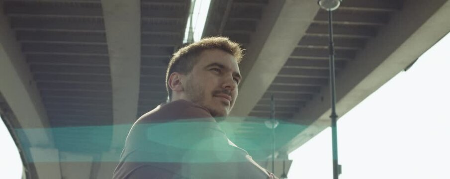 Low angle anamorphic shot of young male athlete in sportswear standing outdoors and doing warmup exercises before training
