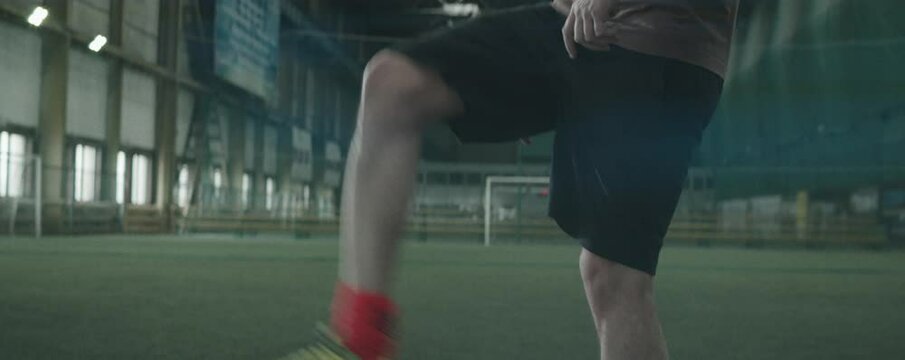 Anamorphic tilt up shot of professional male athlete in sportswear juggling ball on indoor football field