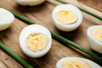 Halves of boiled chicken eggs with green onion pods on a wooden background.