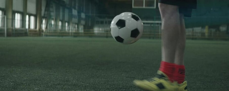 Anamorphic low section shot of legs of professional soccer player in sportswear juggling ball on indoor football field