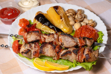 Pork shashlik with lettuce and baked vegetables on a white plate. Grilled meat on skewers. Lunch in nature