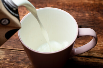 Milk is poured into a cup on a brown wooden background.