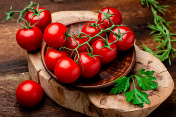 Branch of fresh cherry tomatoes with greens on a brown wooden background.